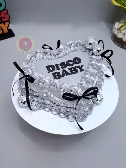 A "Disco Baby" heart-shaped vintage cake in shimmering silver with black ribbons and mini disco balls.