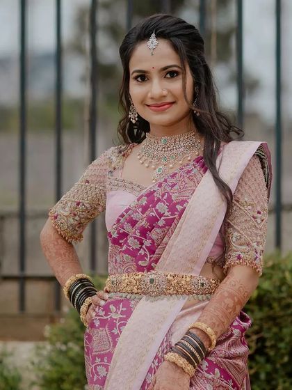 A bride looking elegant in her magenta and pink silk saree. The heavily embroidered blouse and traditional gold jewelry create a rich, festive look perfect for a wedding celebration.