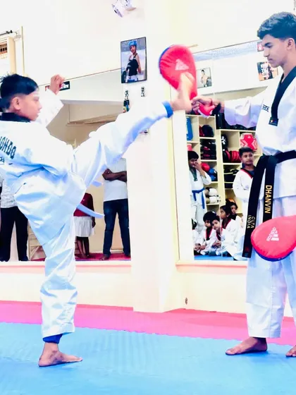 A student practices a high kick on a target held by a senior. This drill helps improve accuracy, height, and power.