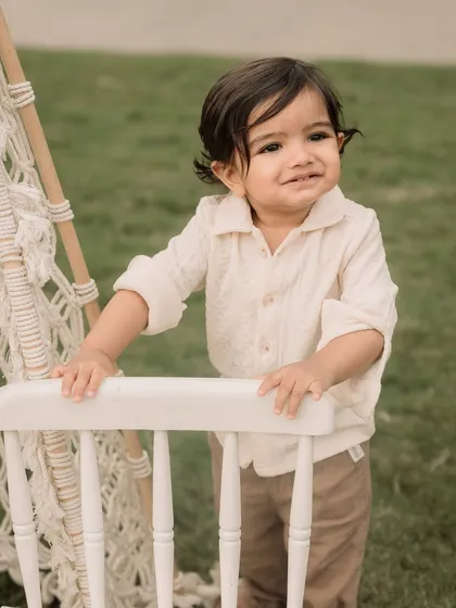 A sweet toddler portrait taken during an outdoor session, with a boho-style chair as a prop.