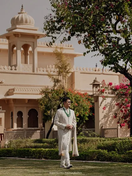 The groom stands in the lush gardens of The Oberoi Udaivilas, a perfect portrait capturing the calm before the ceremony.