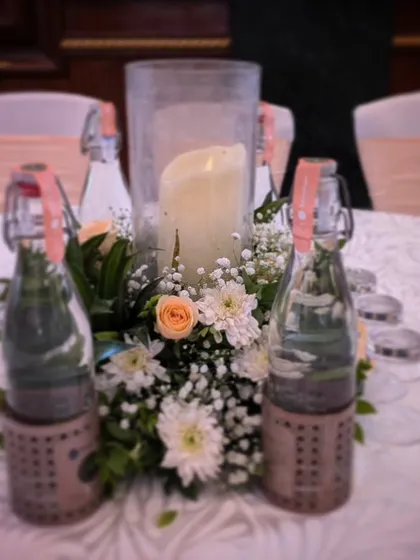 A charming and rustic table centerpiece, with a central candle surrounded by small flowers and greenery, perfect for an intimate and relaxed celebration.