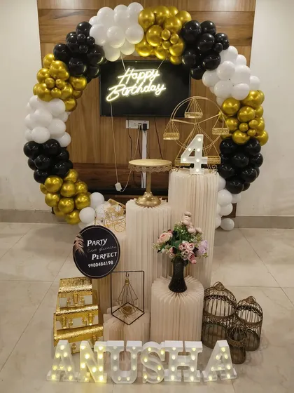 A classic black, white, and gold theme is always a stylish choice for any age. This decoration includes a full balloon ring, a central neon 'Happy Birthday' sign, a light-up number '4', and multiple pedestals for the cake and other decorative elements like a miniature Ferris wheel.