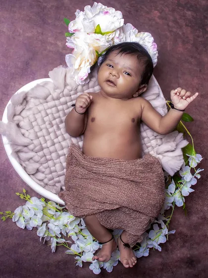An awake baby boy lies in a heart-shaped bowl, looking up with curiosity. This pose shows a different side of newborn photography, focusing on their alert expressions.