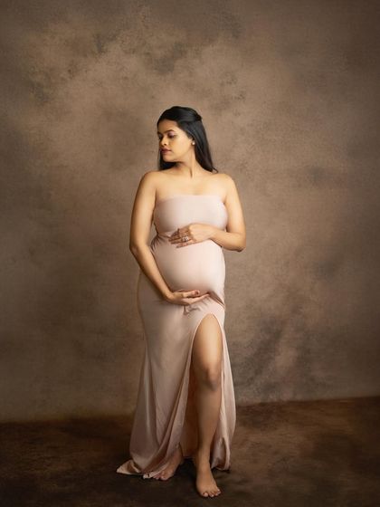 The simplicity of this portrait is what makes it so powerful. A classic bodycon gown in a soft nude tone highlights the perfect shape of the baby bump against a fine-art, textured backdrop.