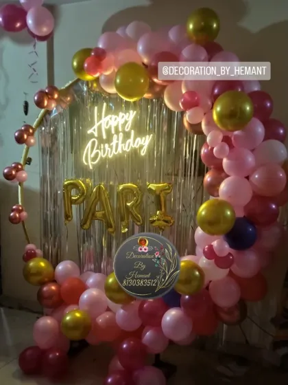 A circular ring backdrop decorated with pink, red, and gold balloons for Pari's birthday. The center features a silver fringe curtain, a "Happy Birthday" neon sign, and foil letters spelling out the name.