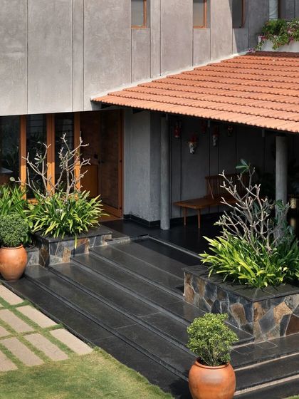 The entrance to this 'House in the Tropics' in Chennai features a modern concrete form juxtaposed with a traditional tiled roof and lush planters.