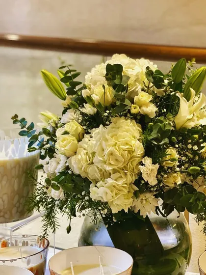 A classic bouquet is always a good choice. This arrangement features a full bunch of white hydrangeas, elegant white lilies, and soft roses, accented with fresh eucalyptus leaves and baby's breath in a simple glass vase.