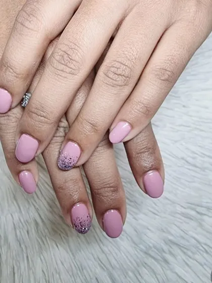 A simple yet stunning design featuring a soft pink gel polish on natural oval nails. The ring finger has a beautiful fade into purple glitter for a subtle accent.