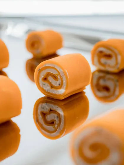 Orange and cream cheese pinwheels with a beautiful swirl, reflecting the simple elegance of the Valentino brand. The mirrored reflection adds a touch of sophistication to the presentation.