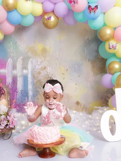 With cake-covered hands and a happy smile, this one-year-old is fully enjoying her cake smash session. This shot captures the messy, joyful reality of a first birthday.