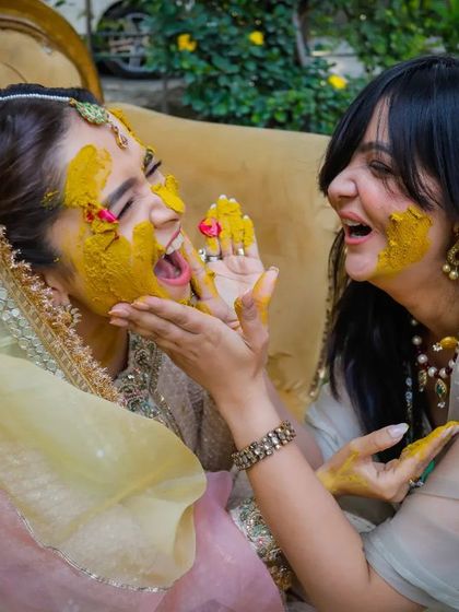 A candid moment of laughter between the bride and her friend as they apply haldi to each other.