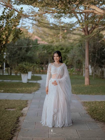 A full-length portrait of the bride in her elegant white reception lehenga, smiling happily.