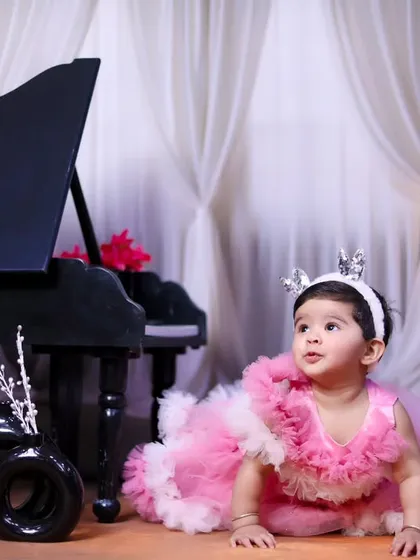 A baby girl in a fluffy pink dress exploring our elegant piano setup.