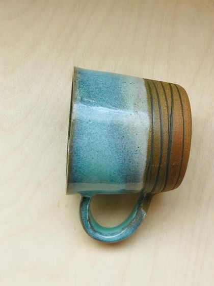 A side view of the Flow Mug, showing the carved lines on the base and the way the blue glaze drips down to meet the raw clay.