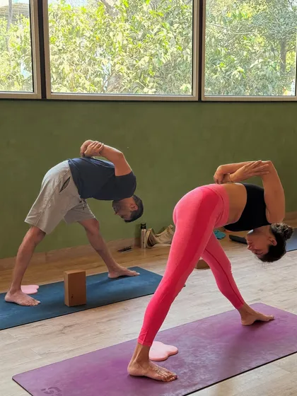 Two members practicing a bound triangle pose, demonstrating strength, balance, and flexibility. The use of a block shows how we adapt poses for all levels.