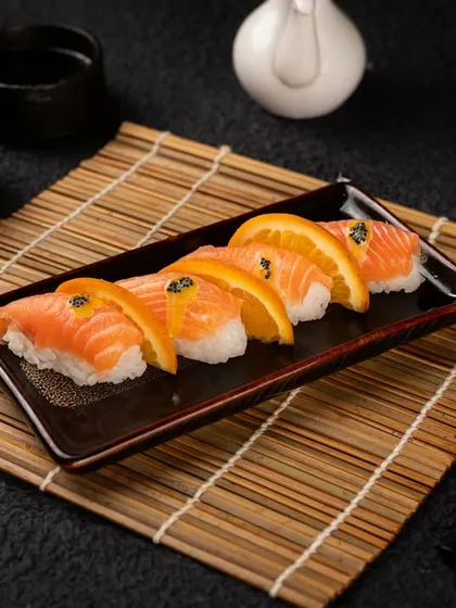 A beautifully styled shot of salmon and orange nigiri on a bamboo mat. This type of photography is perfect for a restaurant's main gallery or online menu.