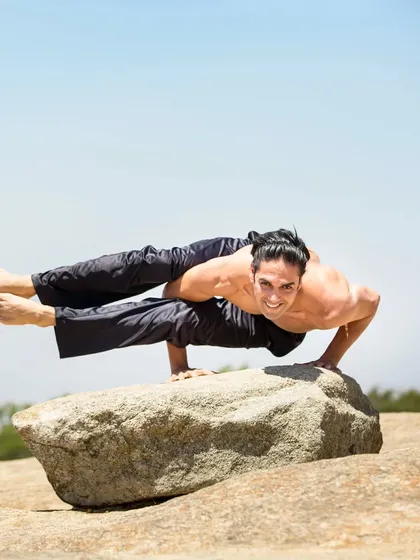 A stunning demonstration of Eka Pada Koundinyasana II in a natural, outdoor setting, connecting the practice with the elements.