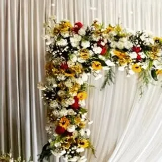 A corner detail of a floral arch, showing a mix of sunflowers, red roses, and white chrysanthemums. This vibrant combination is perfect for a joyful and colorful celebration.