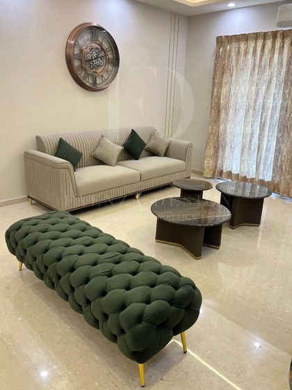 A full view of the living room, showcasing the harmony between the olive green woven bench, the beige sofa, and the nested marble-top coffee tables. The large wall clock adds a classic touch.