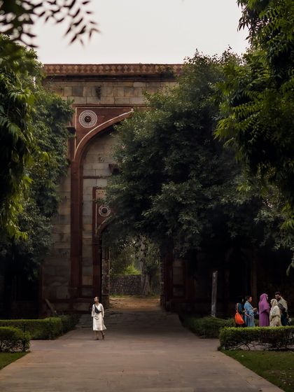 A candid shot capturing a visitor walking through an archway at Humayun's Tomb. The framing by the trees and the contrast between the lone figure and the group creates a nice narrative.