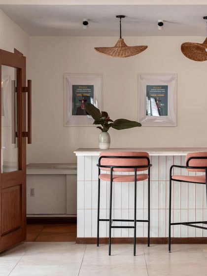 An island counter on the upper floor, designed for pop-ups and workshops. The peach-hued grouting in the white tile cladding adds a subtle pop of color, complemented by fan-shaped rattan pendant lamps.