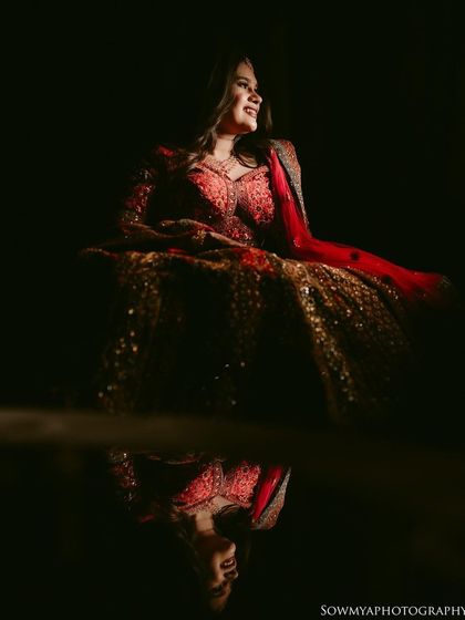 A dramatic portrait of a bride in her red lehenga, with her reflection captured on a glossy surface below. The play of light and reflection is stunning.