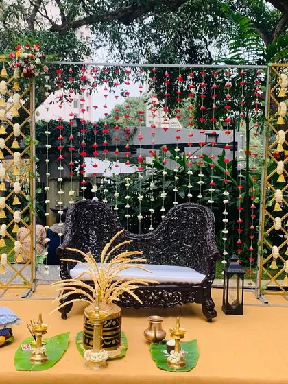 A simple yet elegant outdoor stage for an engagement. The decor features a traditional carved sofa, hanging flower curtains, and side panels with hanging bells for an authentic touch.