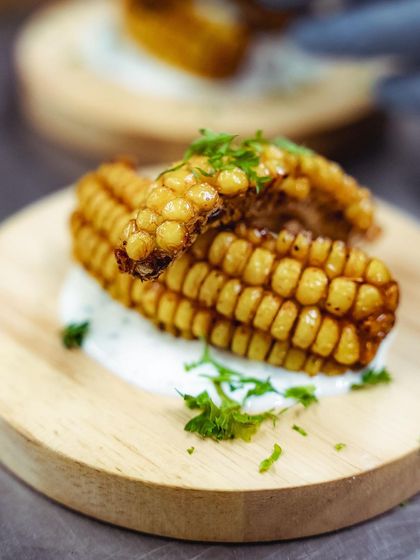 A close-up of our wood-fired corn ribs, served on a dollop of creamy sauce. The char from the oven adds a smoky depth of flavor.