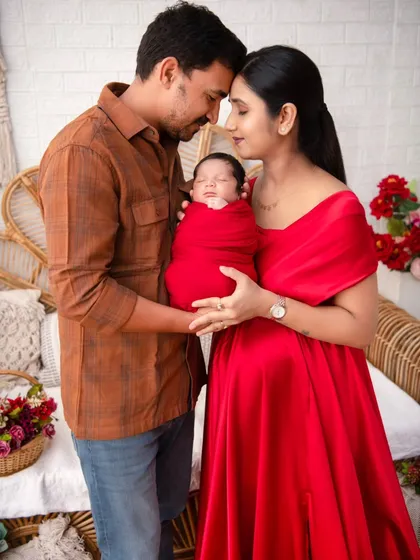 A portrait capturing the profound love of new parents, both gazing at their newborn wrapped in a vibrant red swaddle. This image embodies the beginning of a family's story, a moment of pure connection and adoration that we specialize in preserving.