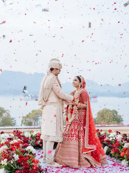 An epic moment of 'just married' bliss. Against the stunning backdrop of Udaipur's lakes, this couple shares their first moments as husband and wife under a shower of celebratory petals.