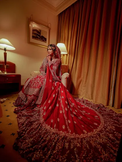 A full portrait of a bride in her magnificent red lehenga with a long train. My goal is to ensure your makeup looks stunning from every angle, complementing the grandeur of your bridal outfit.
