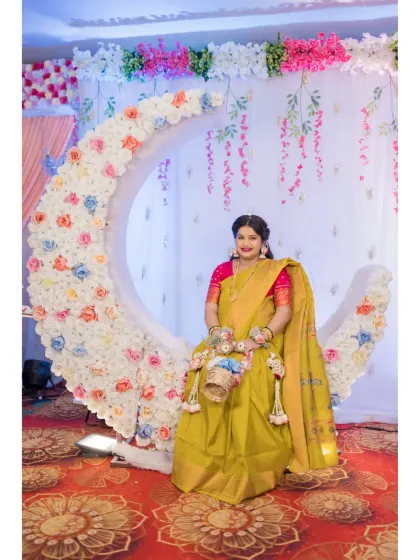 A radiant solo portrait of the mother-to-be at her Dohale Jevan ceremony. She is seated on an elegant, crescent-moon-shaped floral decoration, dressed in a traditional yellow saree, embodying the grace and joy of the occasion.