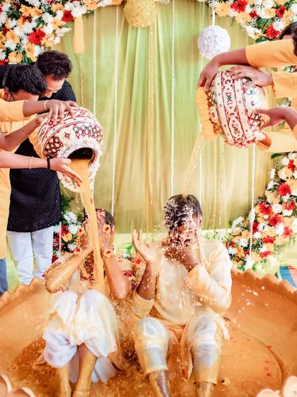 A fun shot of the couple being drenched with turmeric paste by their friends and family during a lively Haldi ceremony.