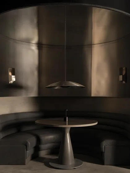 A close-up of a circular booth, where the fusion of raw concrete and sleek leather creates a tactile contrast. The pendant light acts as a focal point, illuminating the table like a stage.