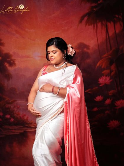 A serene and contemplative portrait of a mom-to-be in a white and pink saree. The soft lighting and painterly background create a dreamy feel.