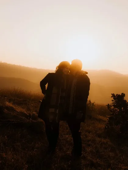 A soft, warm silhouette of the couple against the hazy, golden sunset. This artistic shot is filled with romance and a sense of peaceful intimacy.