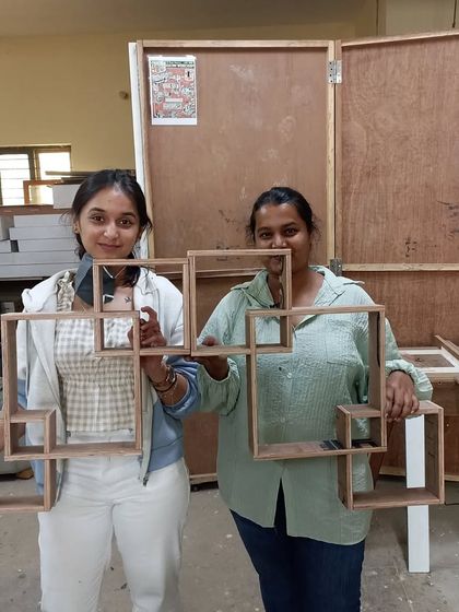 Two design students holding up the interlocking square shelves they created. This is a visually interesting design that is also a great exercise in precision joinery.