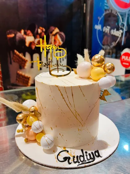 A stylish white and gold birthday cake with delicate gold veining and decorative spheres.
