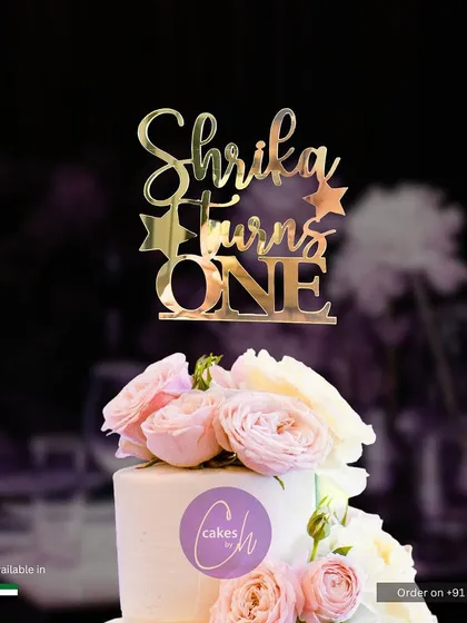 A beautiful mockup of the "Shrika Turns ONE" topper on a cake adorned with fresh pink roses, creating a soft and elegant look.