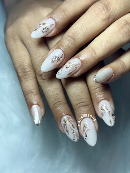 An elegant white manicure with hand-painted gold and silver leafy vines, accented with sparkling rhinestones.