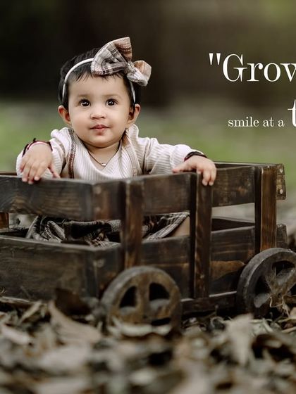 Growing up, one smile at a time. A sweet girl in a wooden wagon looks up, surrounded by autumn leaves.