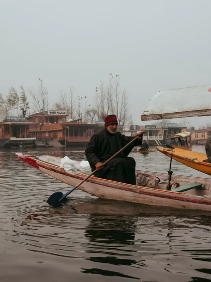 A boatman paddles his shikara past the iconic houseboats of Dal Lake. The scene is full of character, reflecting the unique way of life on the water.