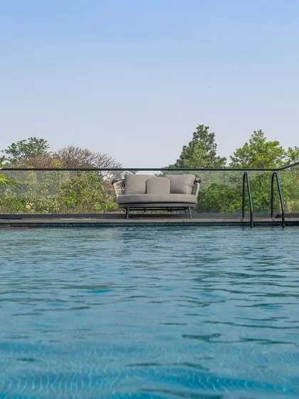 A view across a tranquil swimming pool towards a comfortable seating area on the far side. The landscape is kept minimal, with the expanse of water and the surrounding trees creating a peaceful atmosphere.