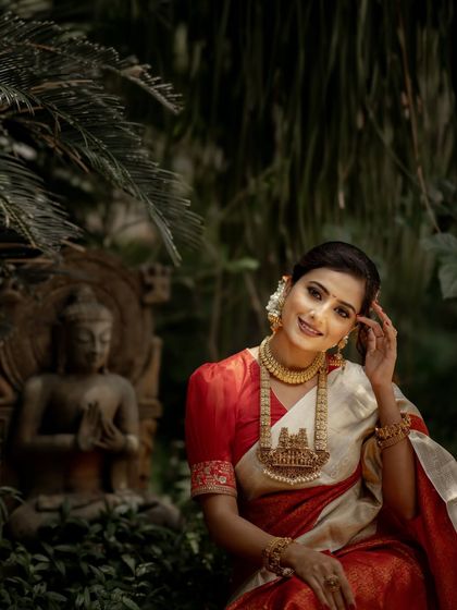 Posed in a serene garden setting, this image captures the peaceful and auspicious nature of a traditional wedding. The red and white silk saree stands out against the natural backdrop.