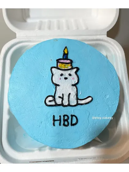 A colorful birthday bento cake with a cute cat wearing a tiny party hat on its head.