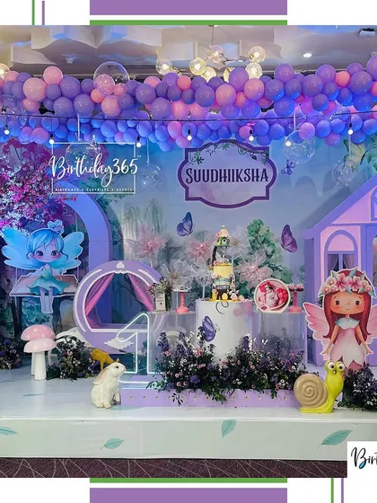 An enchanting fairy-themed birthday party brought to life in dreamy shades of purple. This immersive setup includes a custom fairy house, whimsical character cutouts, oversized mushrooms, and a ceiling adorned with a cascade of balloons and lights.