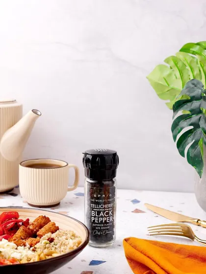 A clean and crisp lifestyle shot of Tellicherry Black Pepper. The modern, bright lighting and minimalist props highlight the premium quality of the spice for a discerning customer.