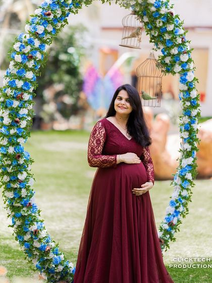 A beautiful, centered portrait of the expectant mother framed by a circular floral arch. This highlights her radiant glow and the elegant maternity gown.