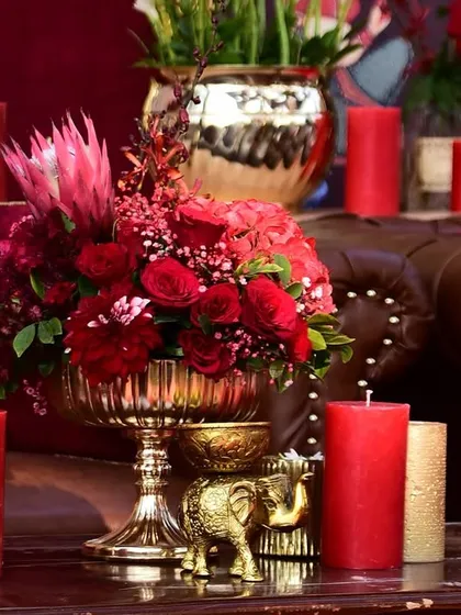 A close-up of a lounge table, showing the rich combination of red floral arrangements, pillar candles, and custom-printed cushions.